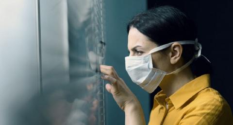 Женщина в маске смотрит в окно Самоизоляция